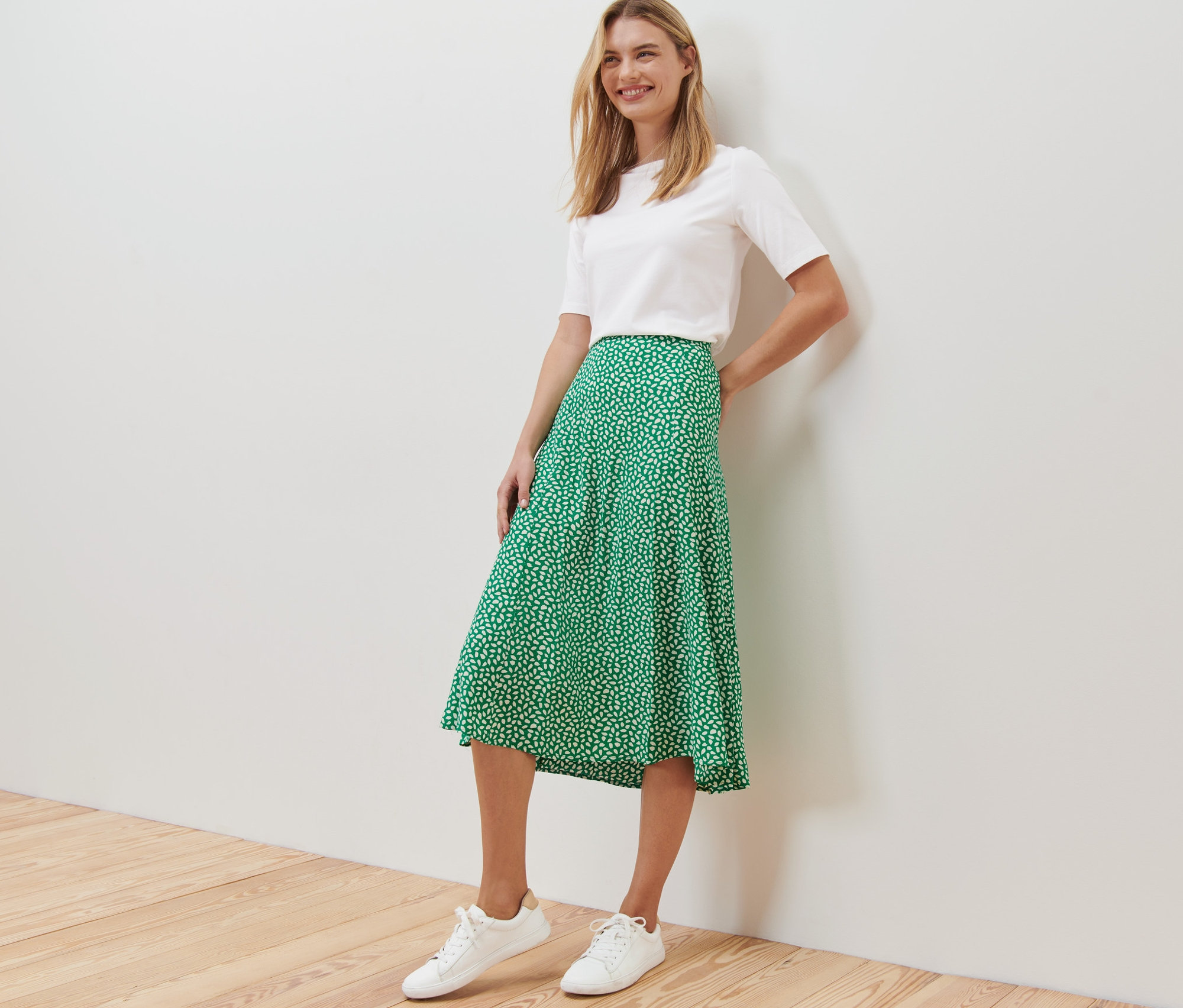 Eine Frau posiert in einem weißen T-Shirt und einem bedruckten grünen Midi-Rock.