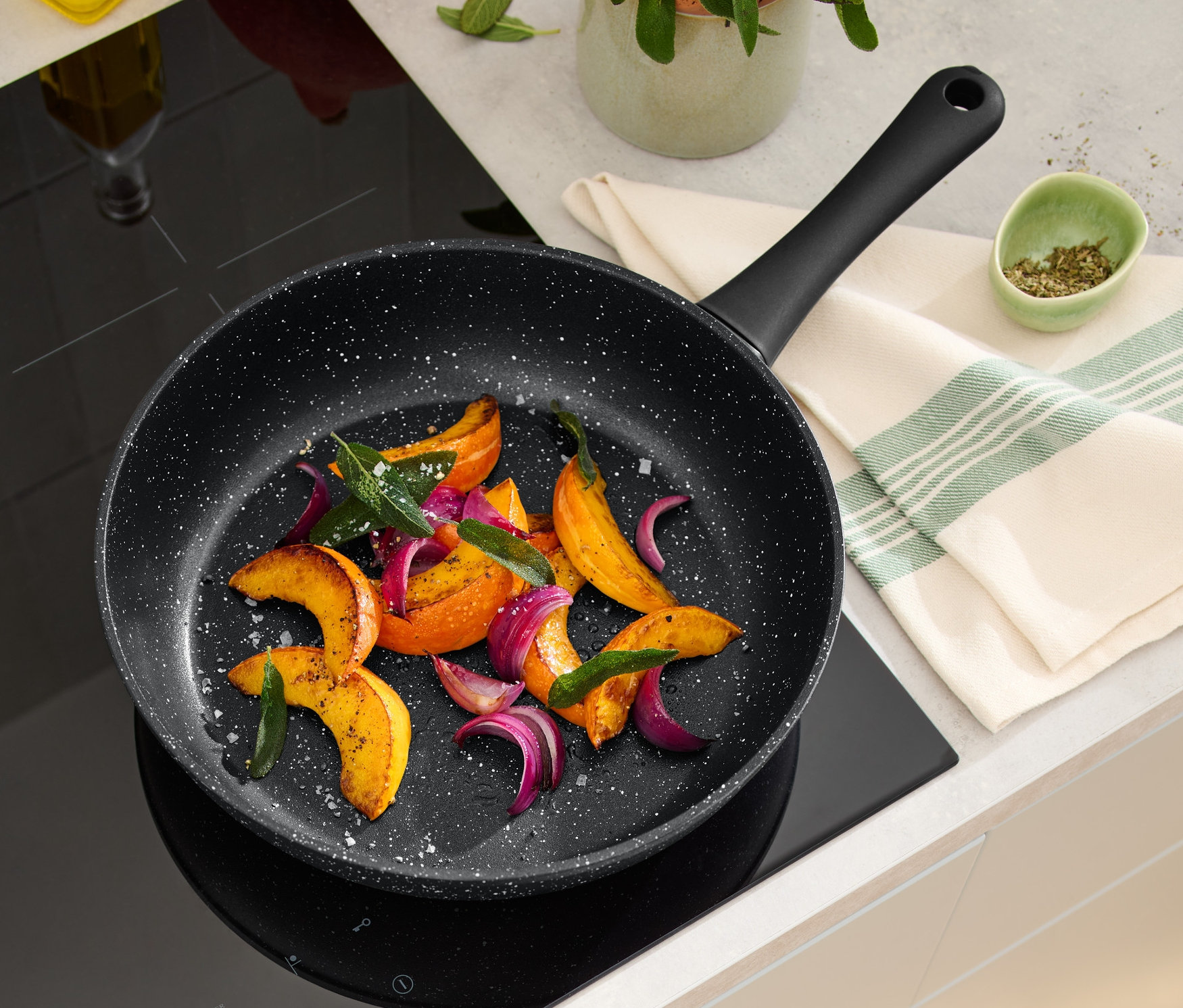 Auf einem Induktionskochfeld steht eine 28 cm Profi-Pfanne in Steinoptik mit gebratenem Gemüse.