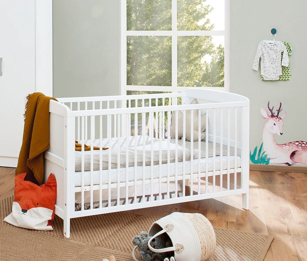 Ein Zimmer mit einem weißen Pinolino Babybett »Viktoria«, neben dem ein weißer Schrank steht und an der Wand eine Hirschdekoration angebracht ist.