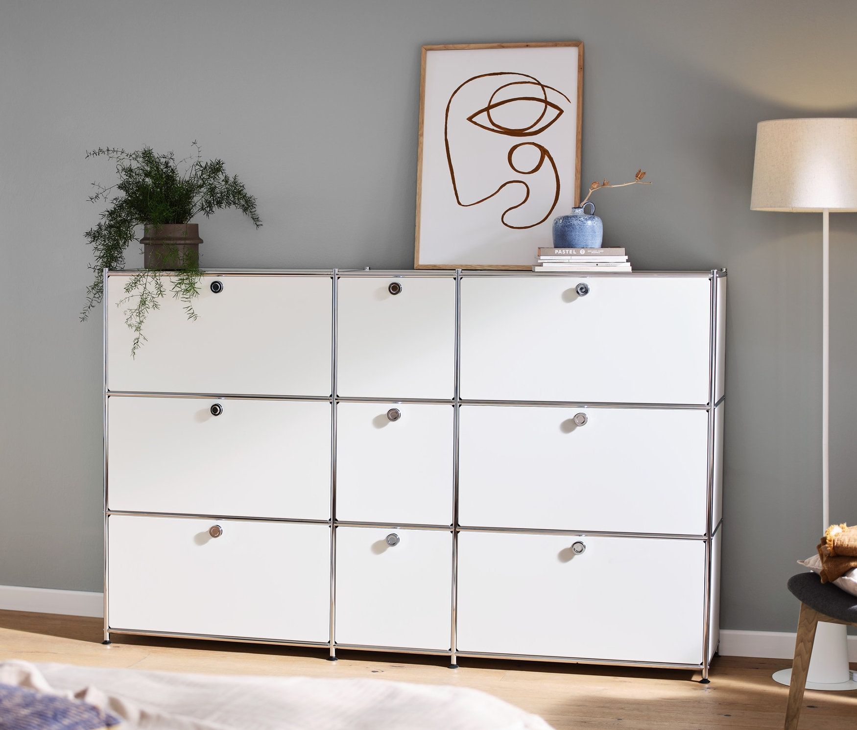 Im Zimmer stehen eine weiße Kommode »CN3« mit 9 Klappen, auf der Deko steht, links ein Konsolentisch und eine Stehleuchte mit Textilschirm.