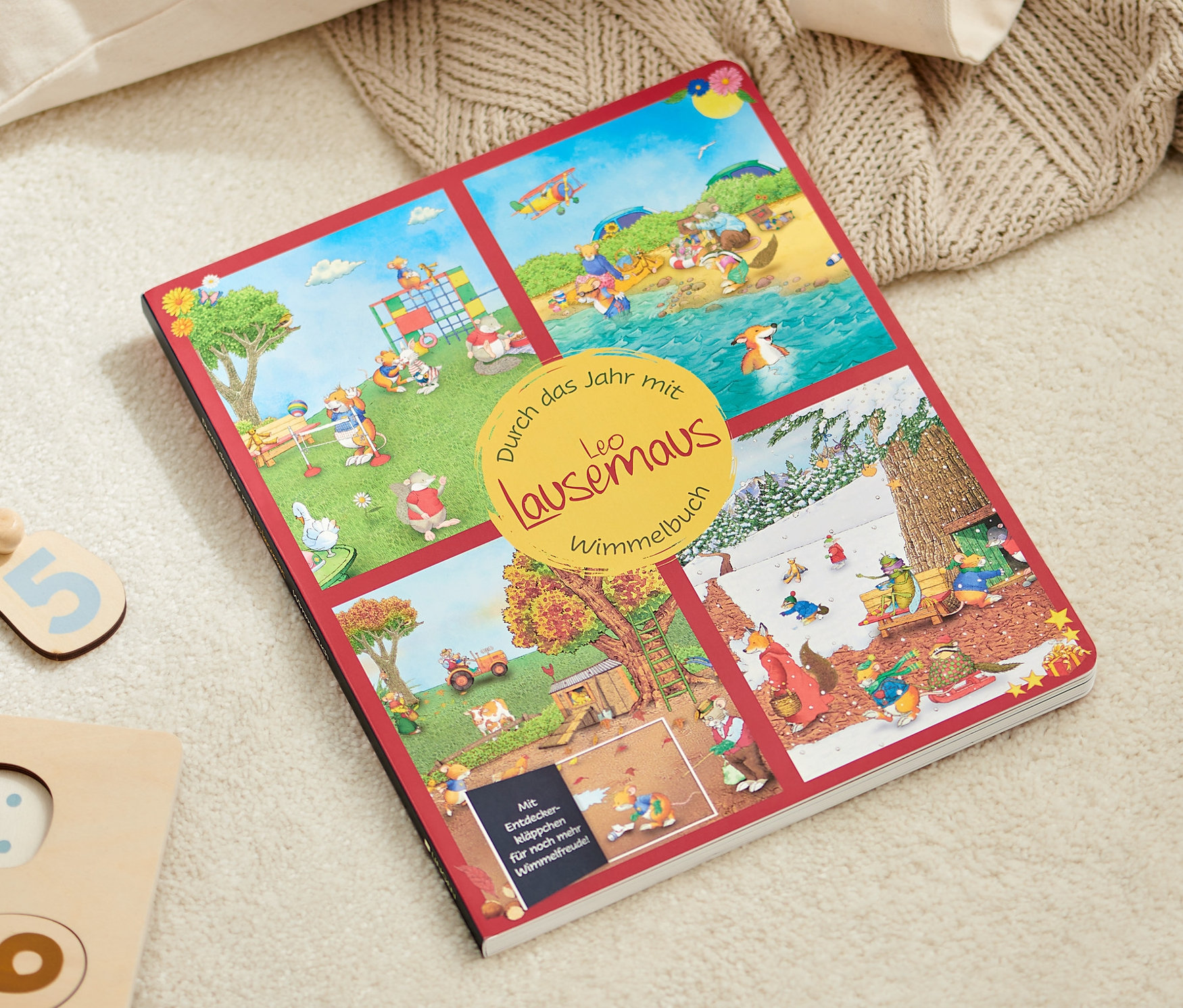 Offenes Wimmelbuch: Durch das Jahr mit Leo Lausemaus liegt auf einem beigen Teppich neben einem Holzpuzzle.