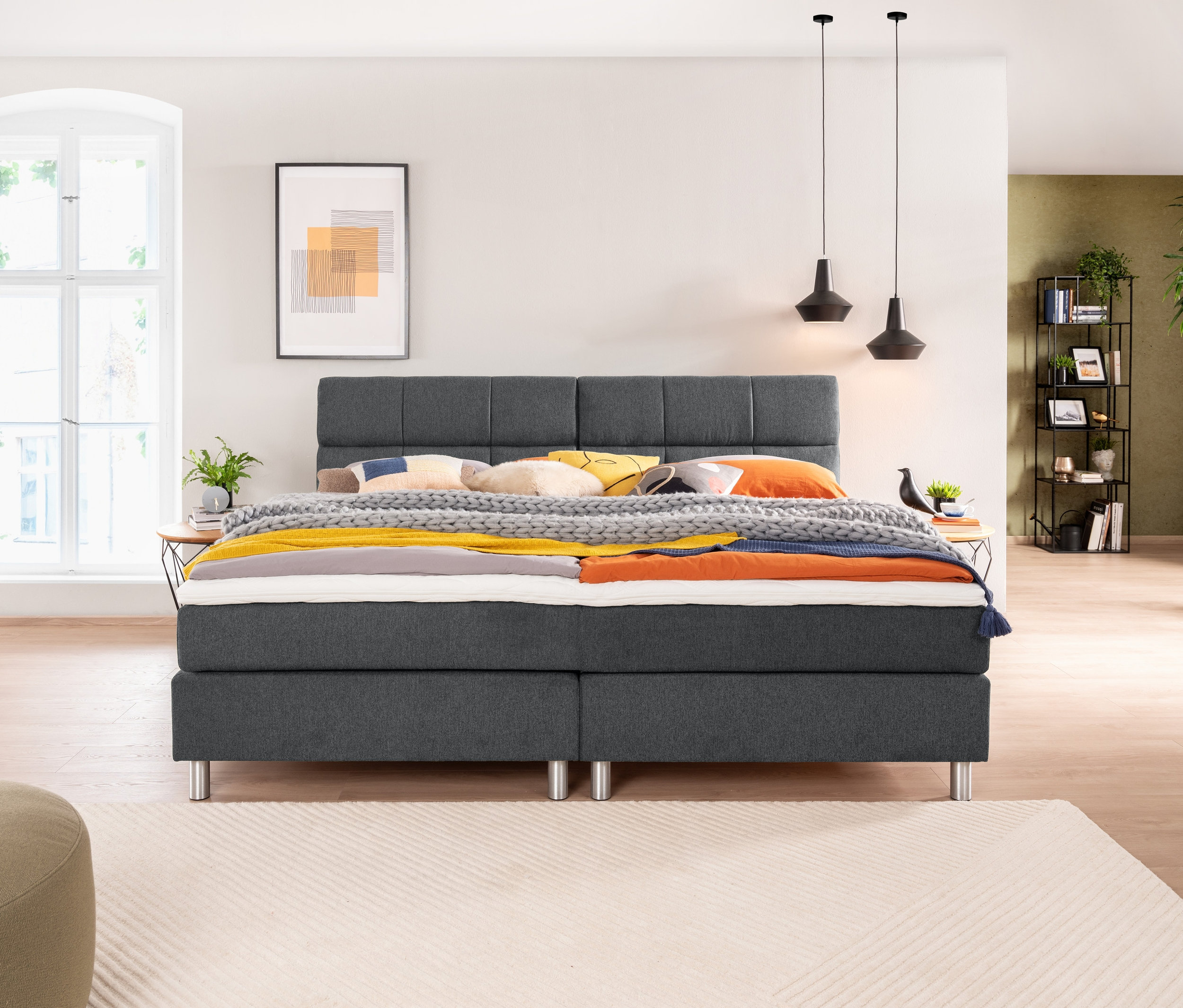 Schlafzimmer mit einem grauen Familienbett, ca. 240 x 200, Nachttischen und Dekoration.