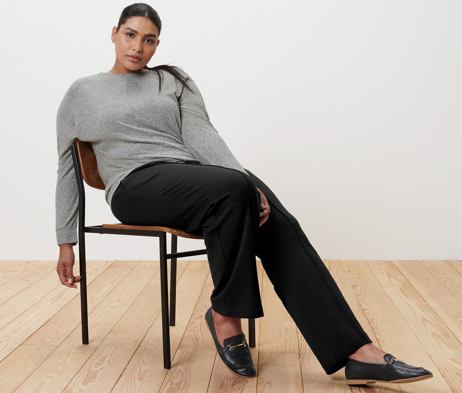 Frau sitzt auf einem Stuhl und trägt eine schwarze Jerseyhose mit Biese, ein Fledermausshirt und Leder-Loafer.