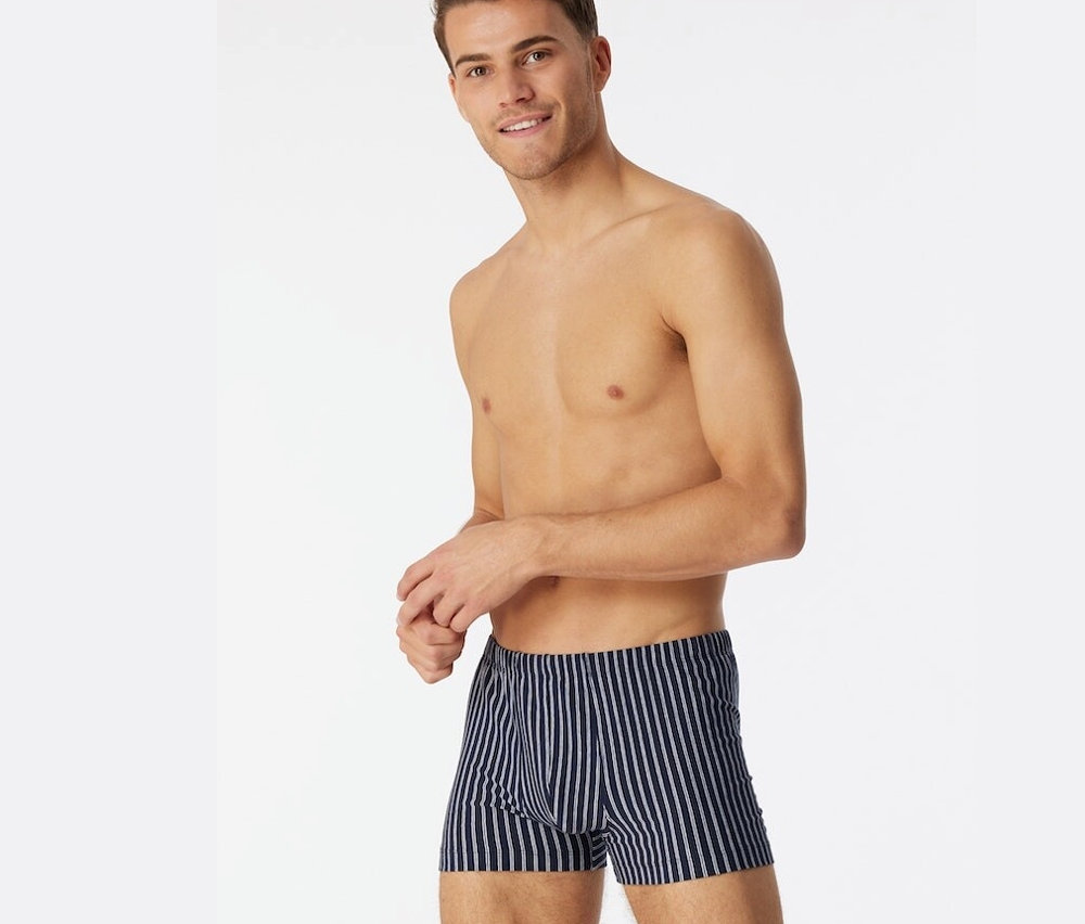 Mann mit freiem Oberkörper trägt dunkelblaue SCHIESSER Shorts mit Bio-Baumwolle.