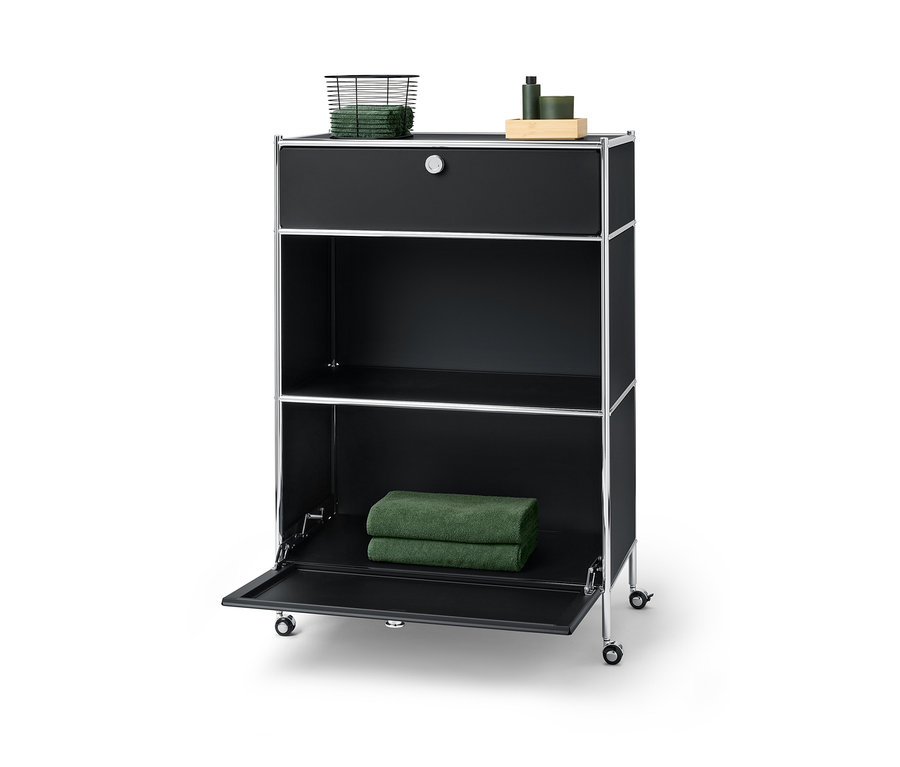 Eine schwarze Kommode Metall »CN3« mit einer Schublade, auf der ein Korb mit Handtüchern liegt, und einem Klappfach, auf dem zwei Handtücher liegen.