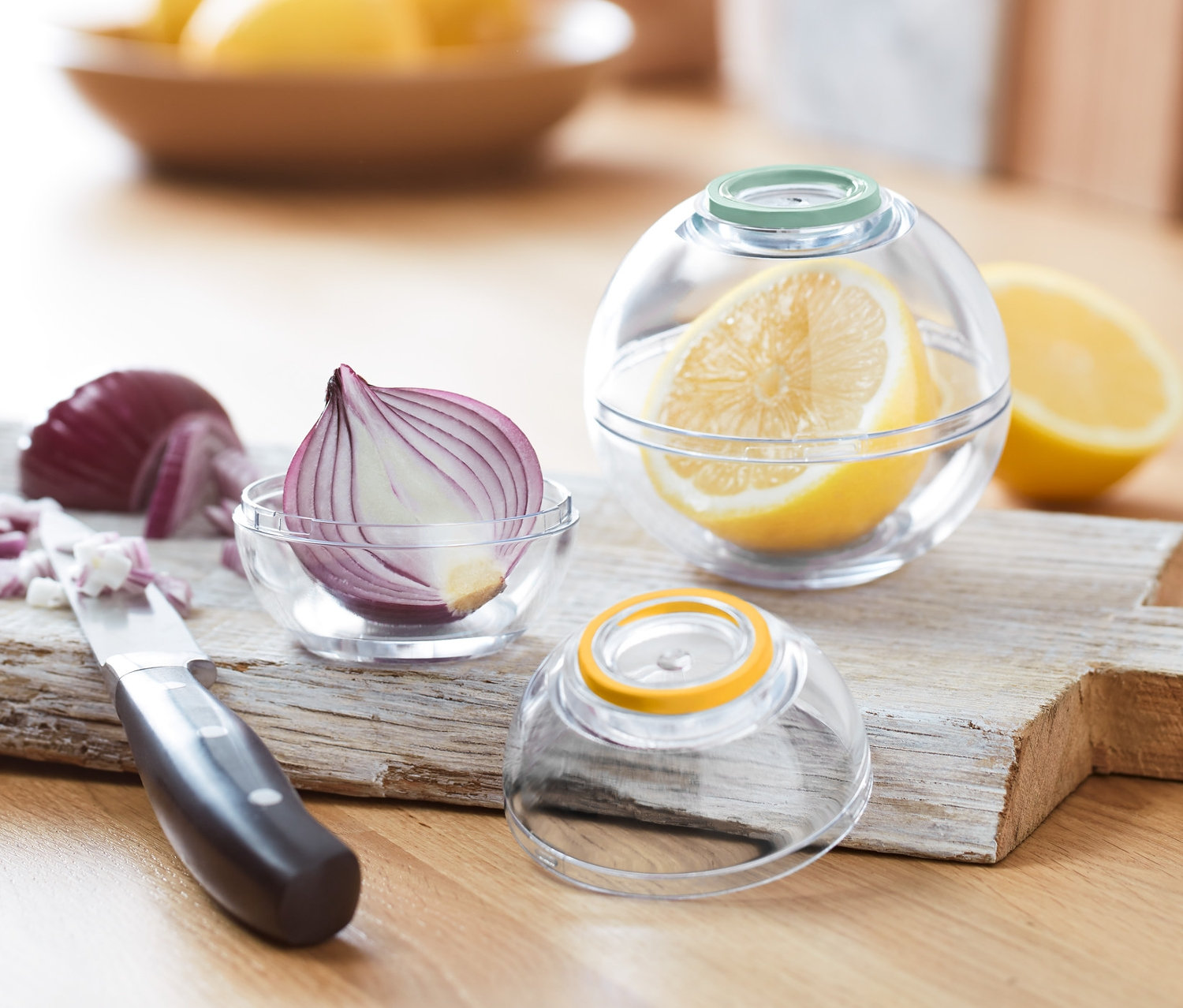 Halbe rote Zwiebel in Frischhaltekugel, daneben geschnittene Zwiebel und Messer. 2 Frischhaltekugeln.