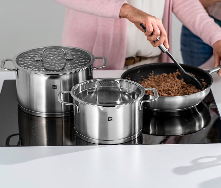 Frau rührt Fleisch in einer Pfanne neben zwei ZWILLING Trueflow Kochtöpfen auf einem Kochfeld.