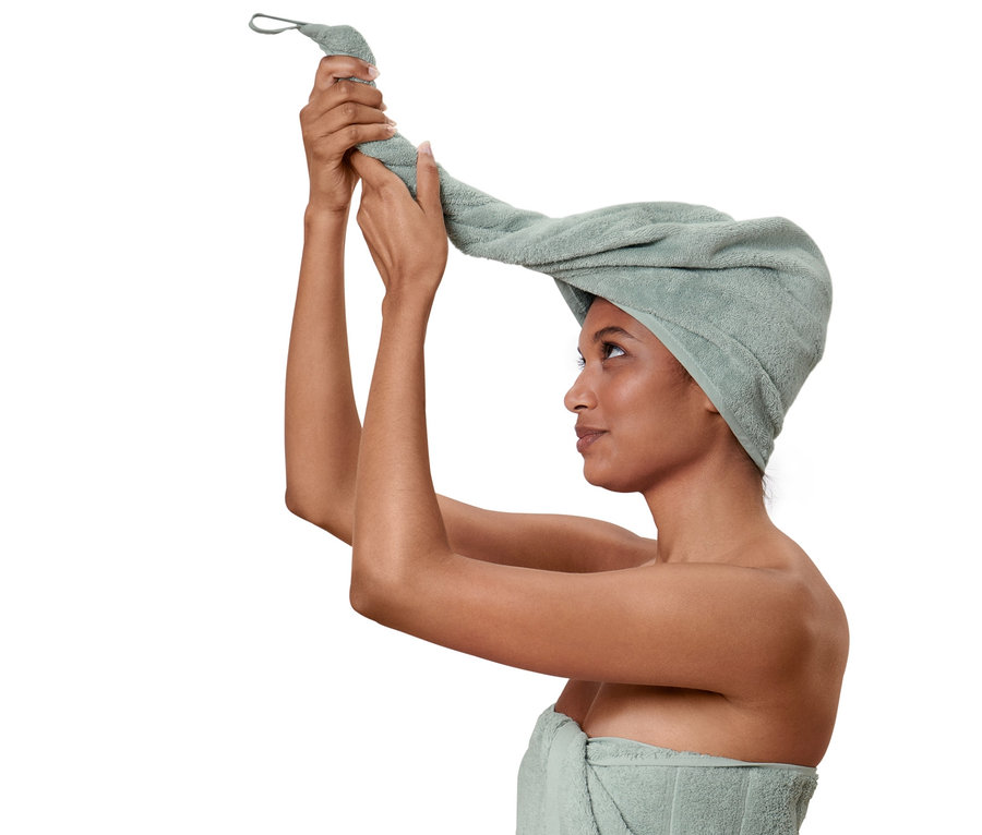 Frau wickelt ein Turban-Handtuch um ihren Kopf, ihr Körper ist mit einem Handtuch umwickelt.