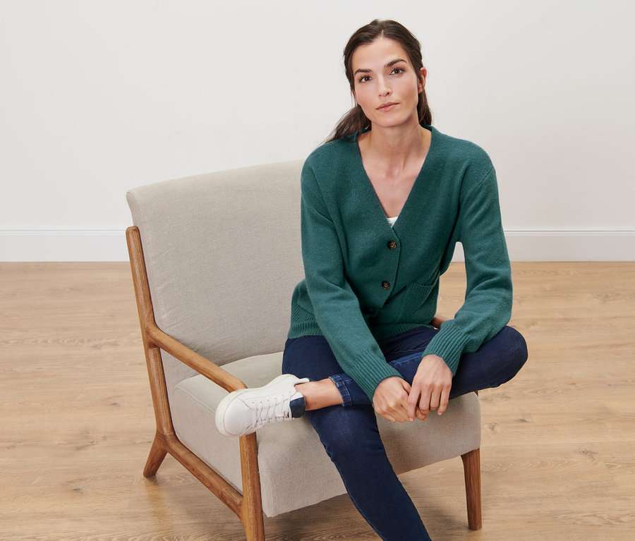 Frau sitzt im Sessel und trägt eine dunkelgrüne Strickjacke mit Wolle.