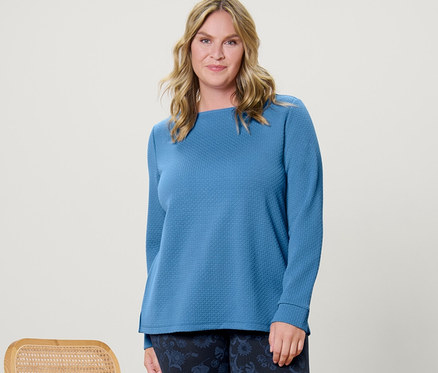 Frau posiert neben einem Stuhl und trägt ein strukturiertes Sweatshirt und bedruckte Leggings.