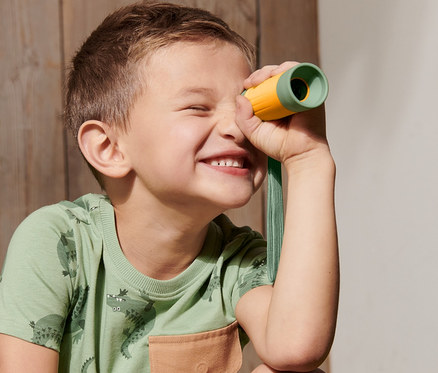 Ein Junge lacht und schaut durch ein Fernrohr.