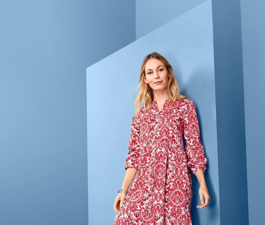 Frau posiert in einem bedruckten Maxikleid vor blauem Hintergrund.