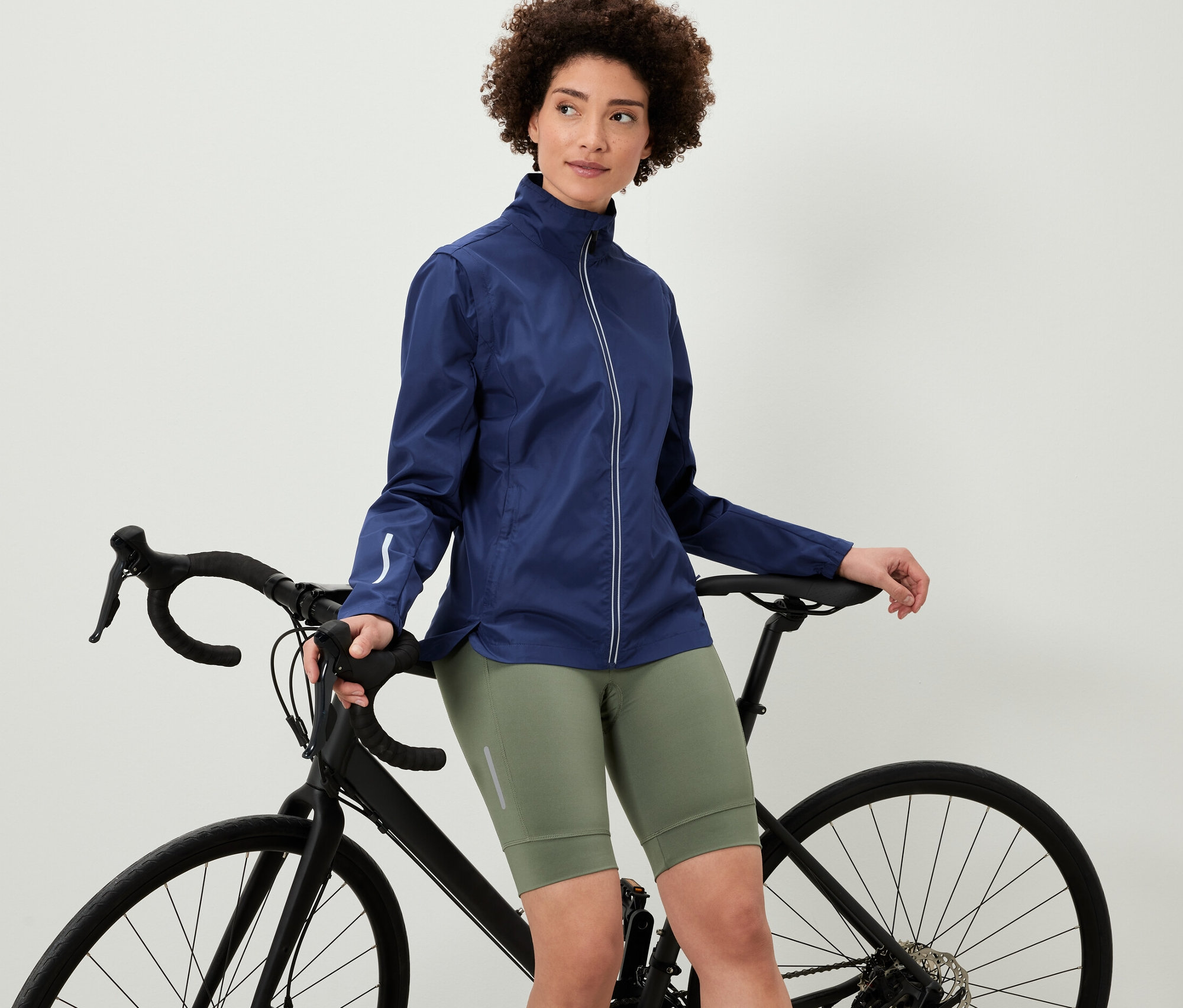 Frau, die sich an ein Fahrrad lehnt, trägt eine 2-in-1-Fahrradjacke.