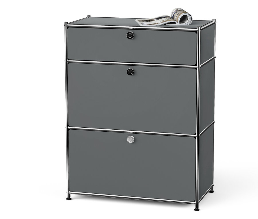 Graue Kommode mit drei Schubladen, Chromrahmen und einer Zeitschrift oben drauf.