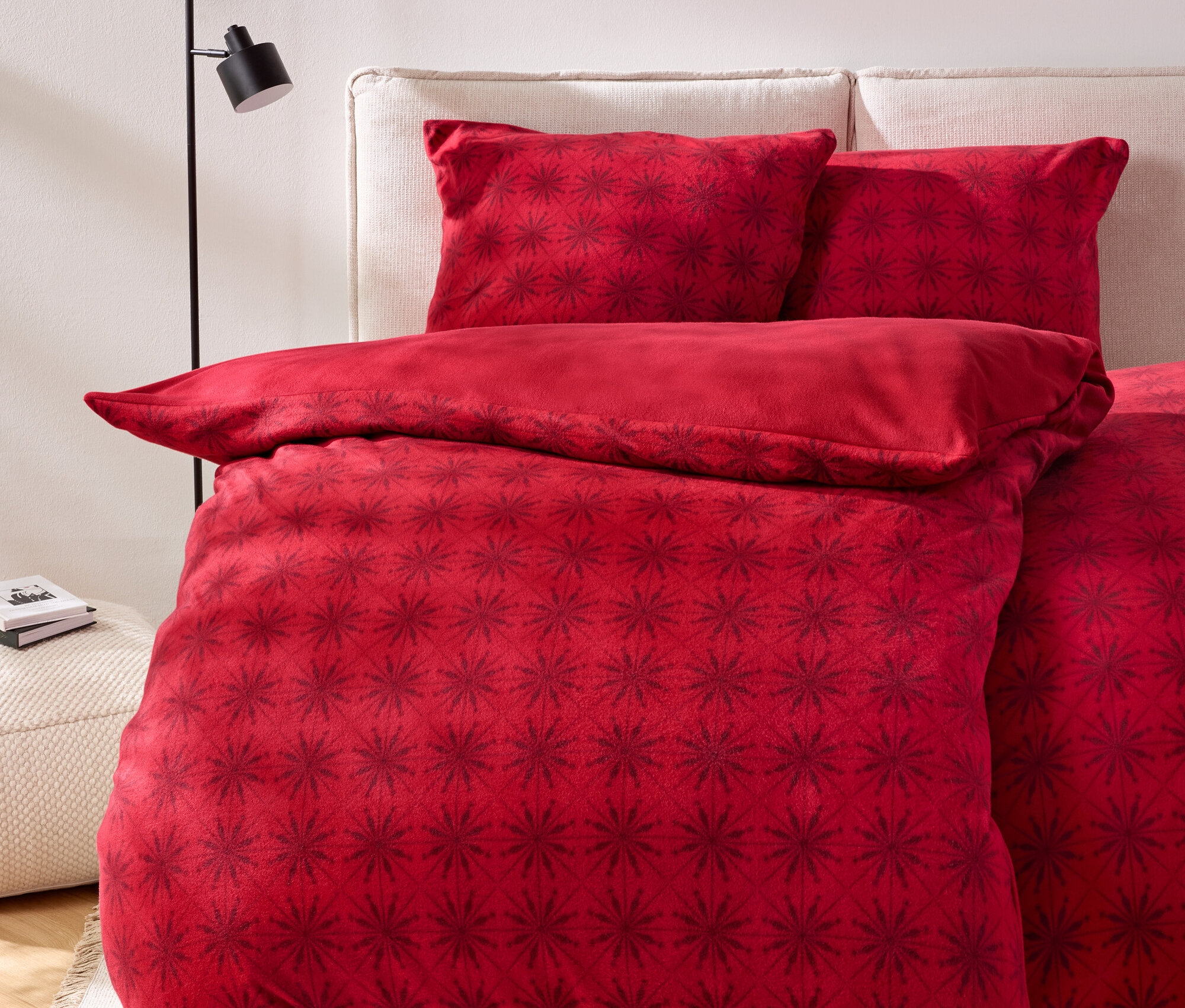 Rote Bettwäsche mit dunklerem Blumenmuster auf einem Bett mit beigem Kopfteil.