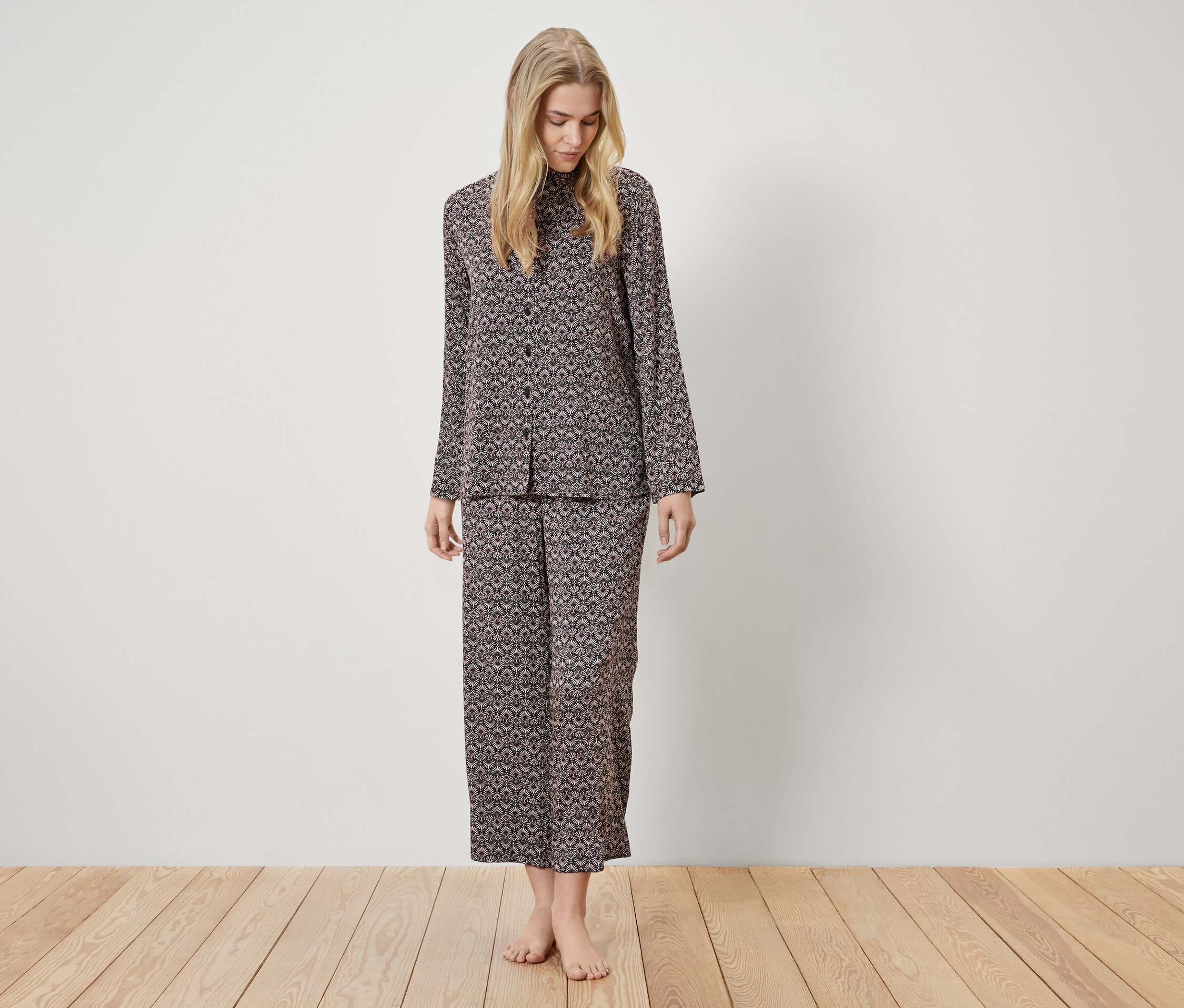 Eine Frau steht und trägt einen braunen Pyjama mit Muster.