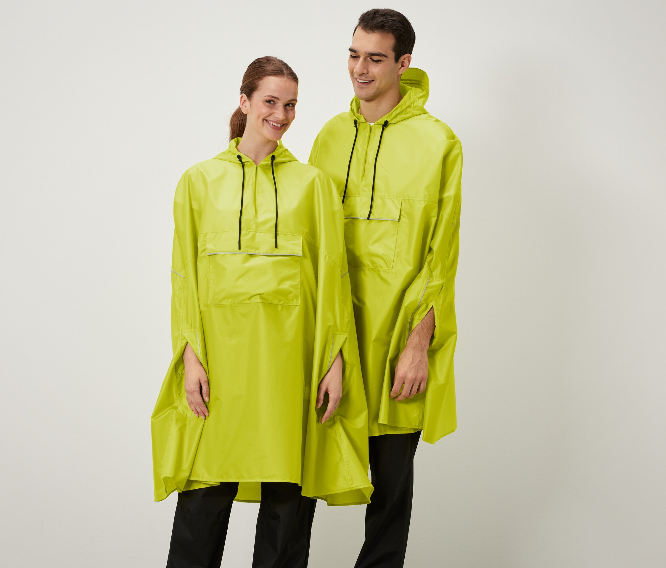 Eine lächelnde Frau und ein Mann posieren in gelben Ponchos mit Kapuze.