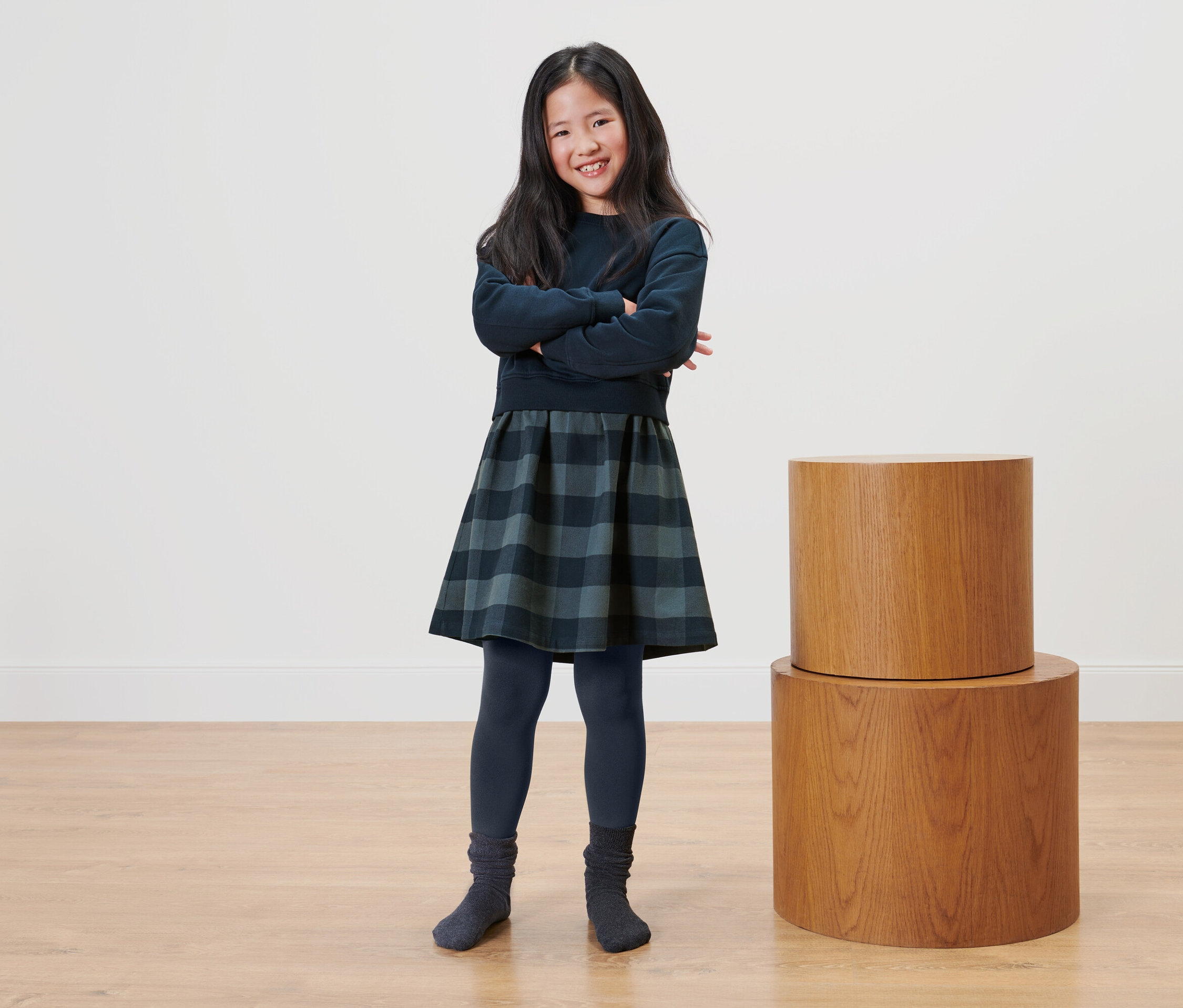 Ein Mädchen steht mit verschränkten Armen neben zwei Holztischen.