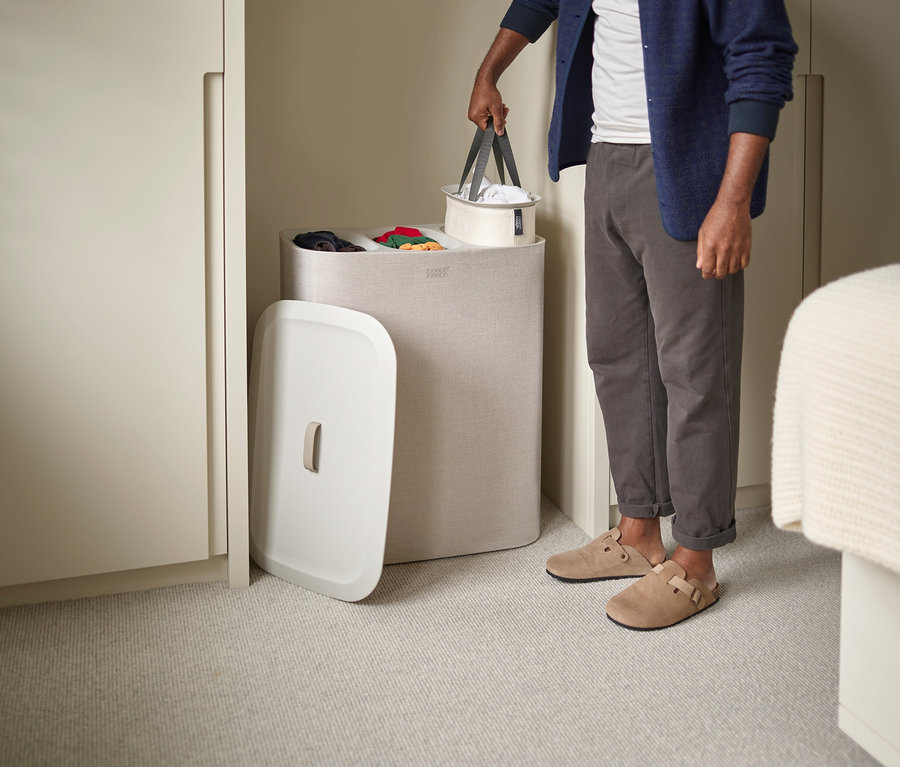 Mann hält Wäschekorb neben einem Wäschebehälter mit Fächern.