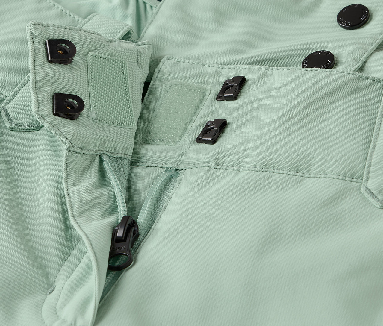 Detailaufnahme einer hellgrünen Hose mit Reißverschluss und Knopfverschluss.
