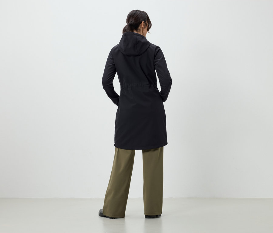 Frau mit dem Rücken zur Kamera trägt einen schwarzen Mantel und eine grüne Hose.