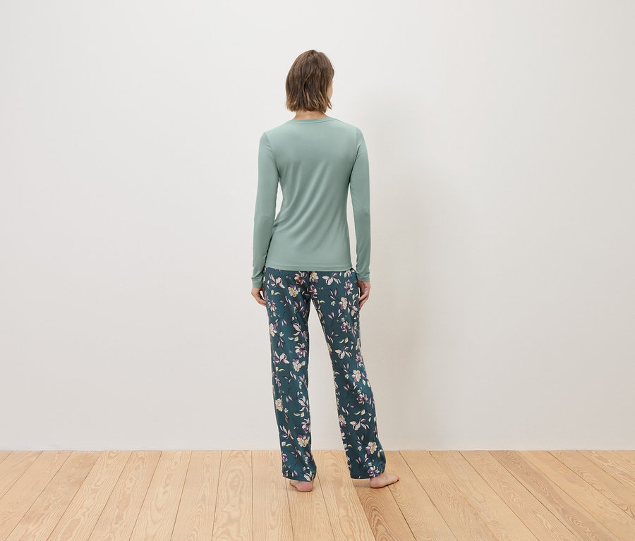 Rückansicht einer Frau mit einem mintgrünen Langarmshirt und einer dunkelgrünen, blumengemusterten Hose.