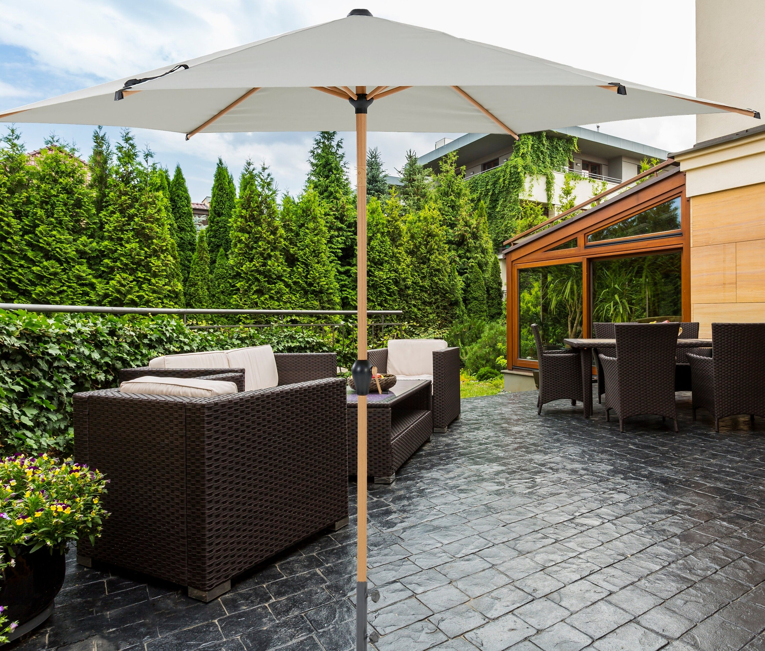 Außenbereich mit braunen Rattanmöbeln und einem grauen Leco Marktschirm in Holzoptik inklusive Abdeckhaube.