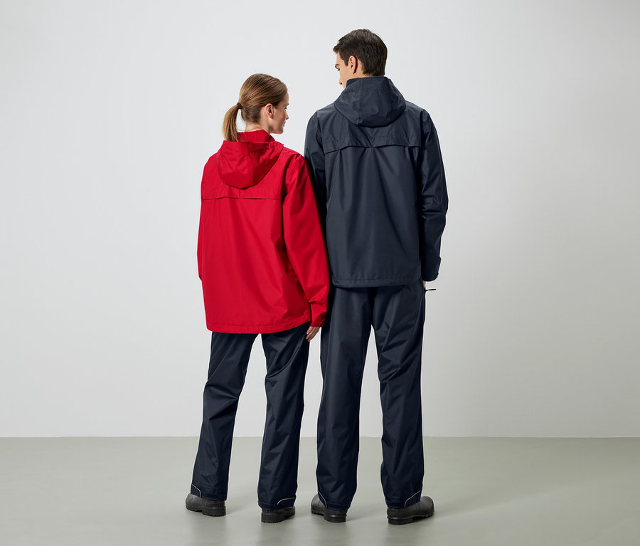 Zwei Personen stehen von hinten in Regenjacken und Regenhosen. Die Frau trägt eine rote Jacke und der Mann eine dunkelblaue Jacke.