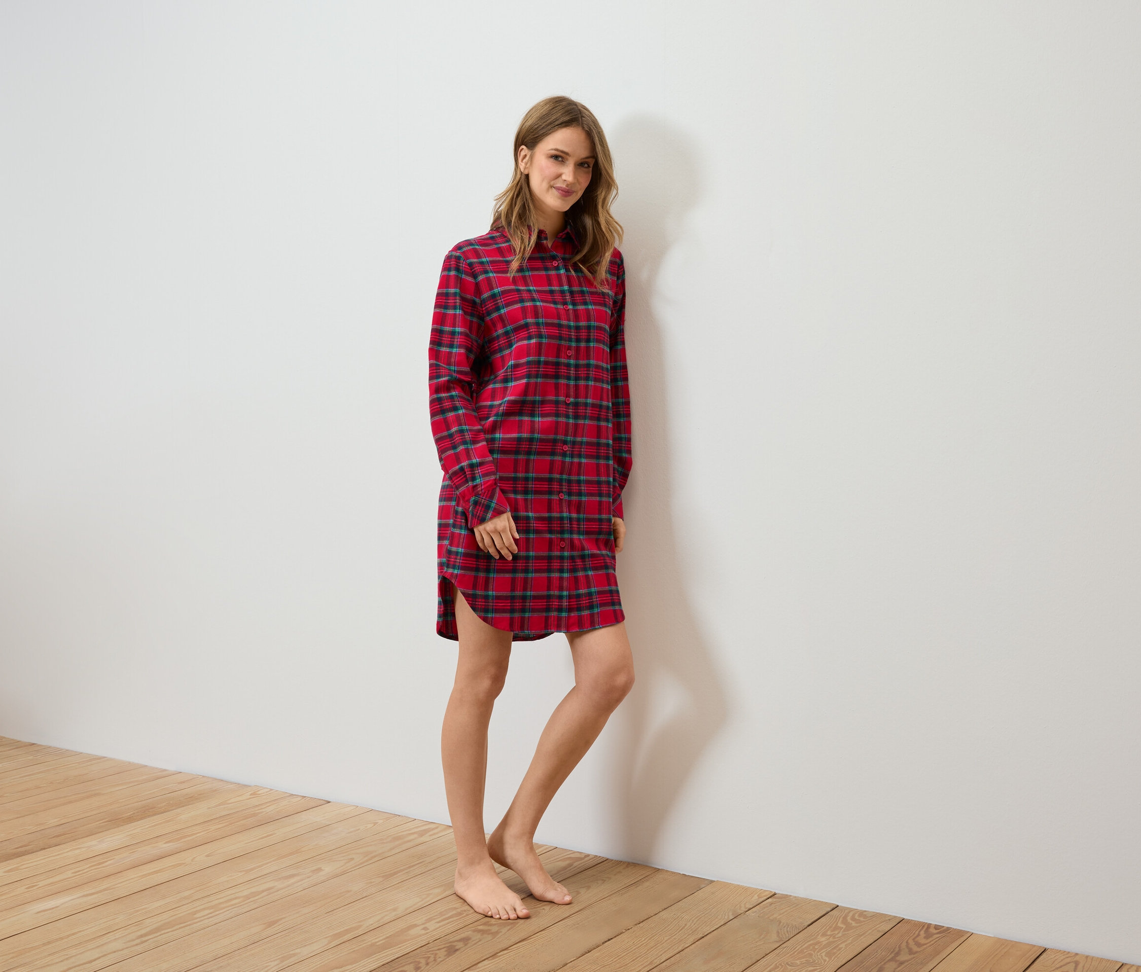 Frau steht und trägt ein rotes kariertes Flanell-Nachthemd.