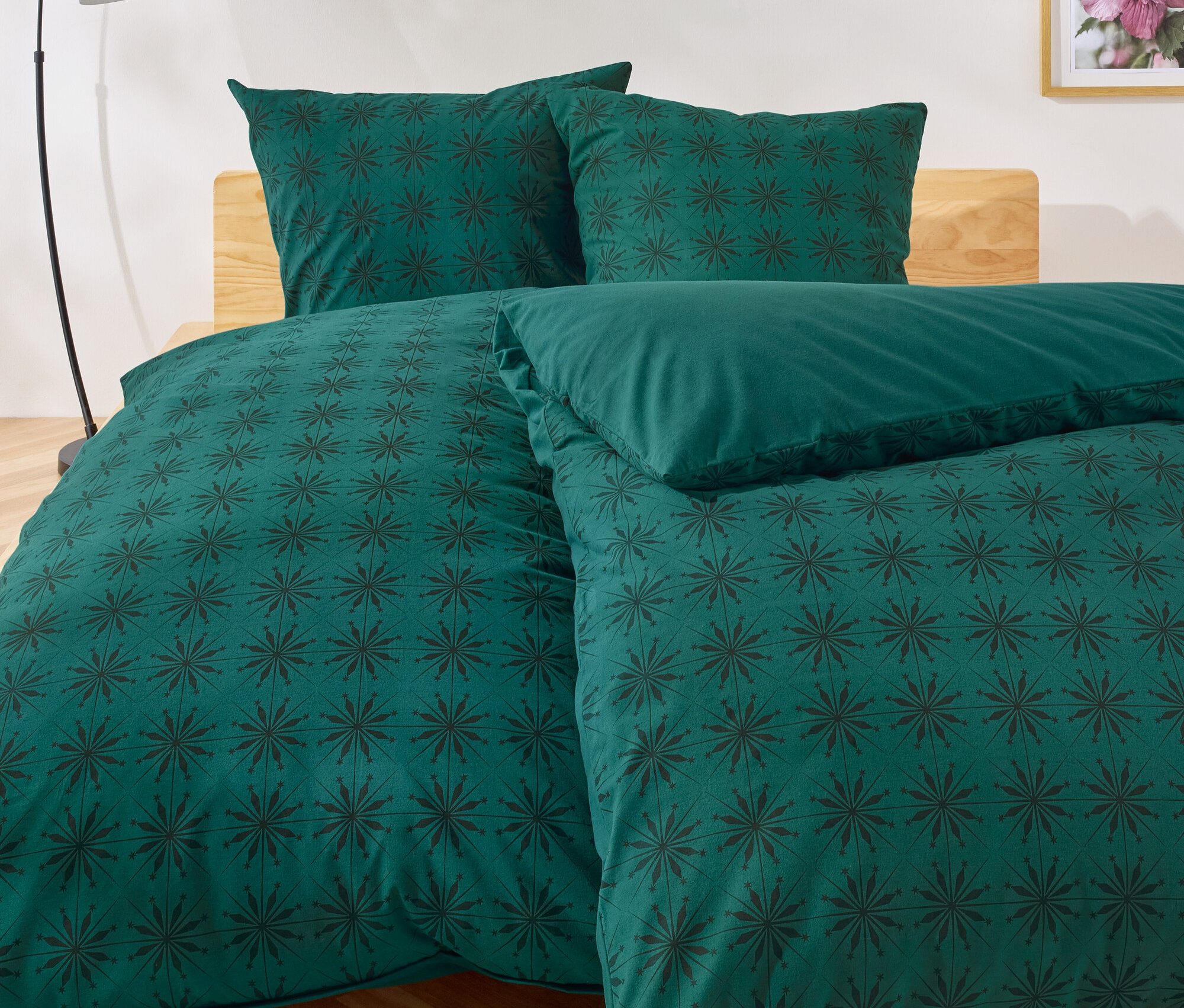 Grüne Bettwäsche mit dunklem Blumenmuster auf einem Bett.