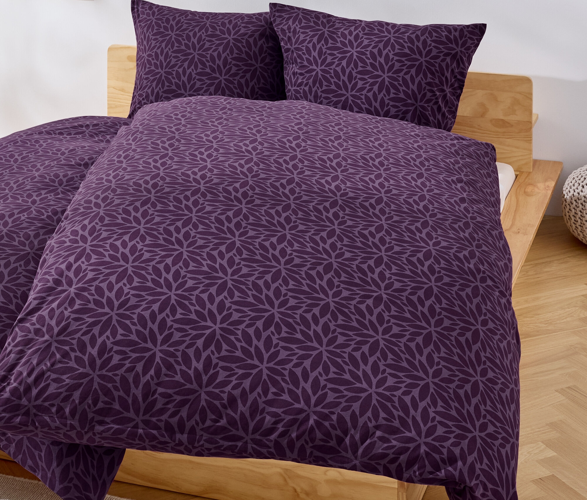 Lila-farbene Bettwäsche mit Blumenmuster auf einem Bett.
