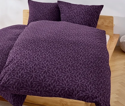Lila-farbene Bettwäsche mit Blumenmuster auf einem Bett.