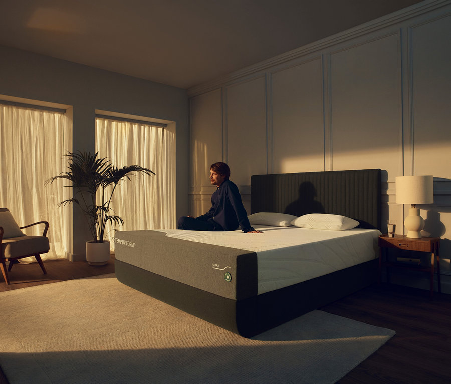 Mann sitzt auf TEMPUR Form™ Plus Matratze, firm, im Schlafzimmer.