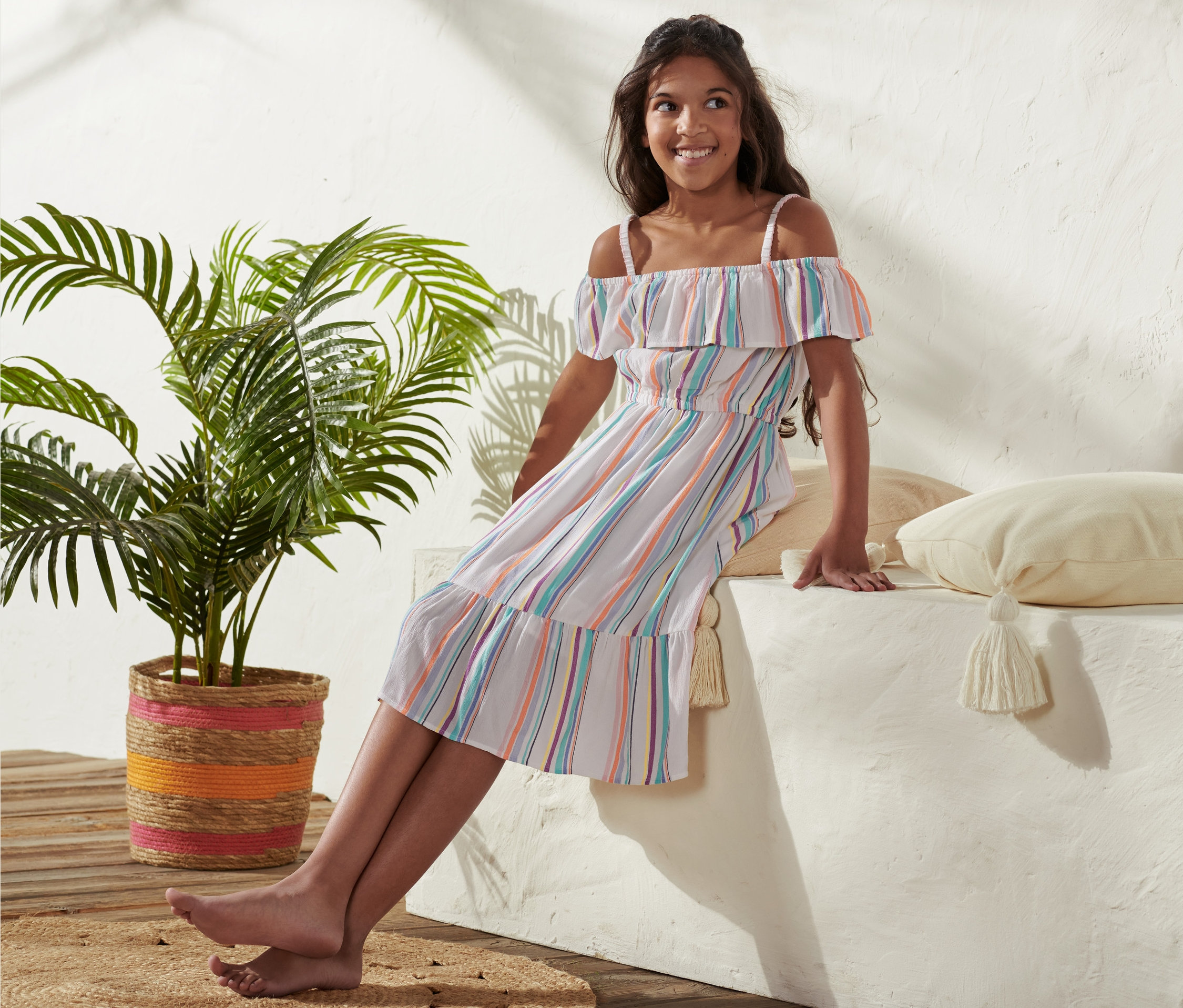 Mädchen sitzt auf einer Mauer und trägt ein Webkleid aus Viskose.