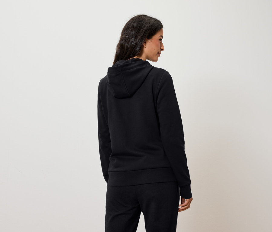 Eine Frau von hinten trägt einen schwarzen Hoodie und eine schwarze Hose.
