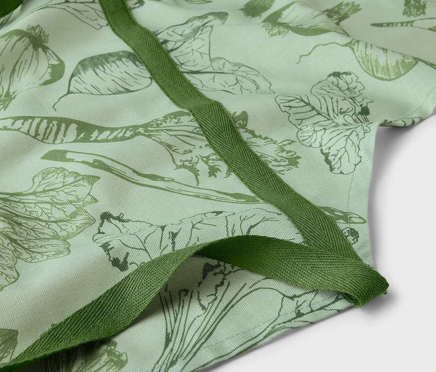 Detailaufnahme einer grünen Schürze mit Gemüseaufdruck und olivgrünen Bindebändern.