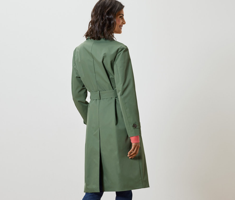 Frau blickt über die Schulter und trägt einen hellgrünen Trenchcoat.