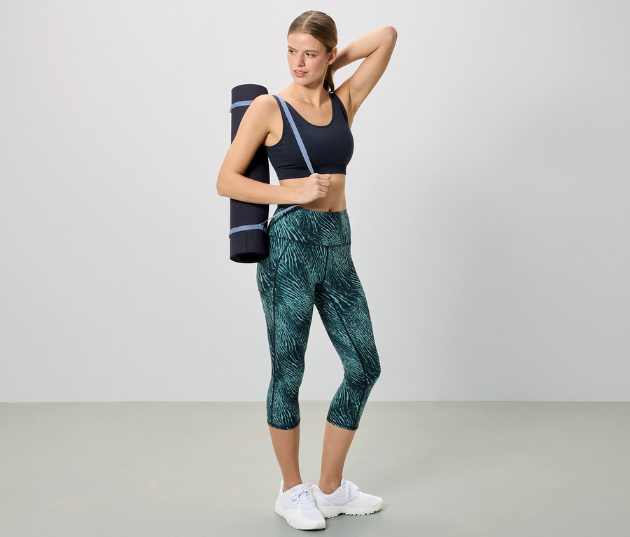 Frau in Sportbekleidung mit einer Yogamatte über der Schulter.