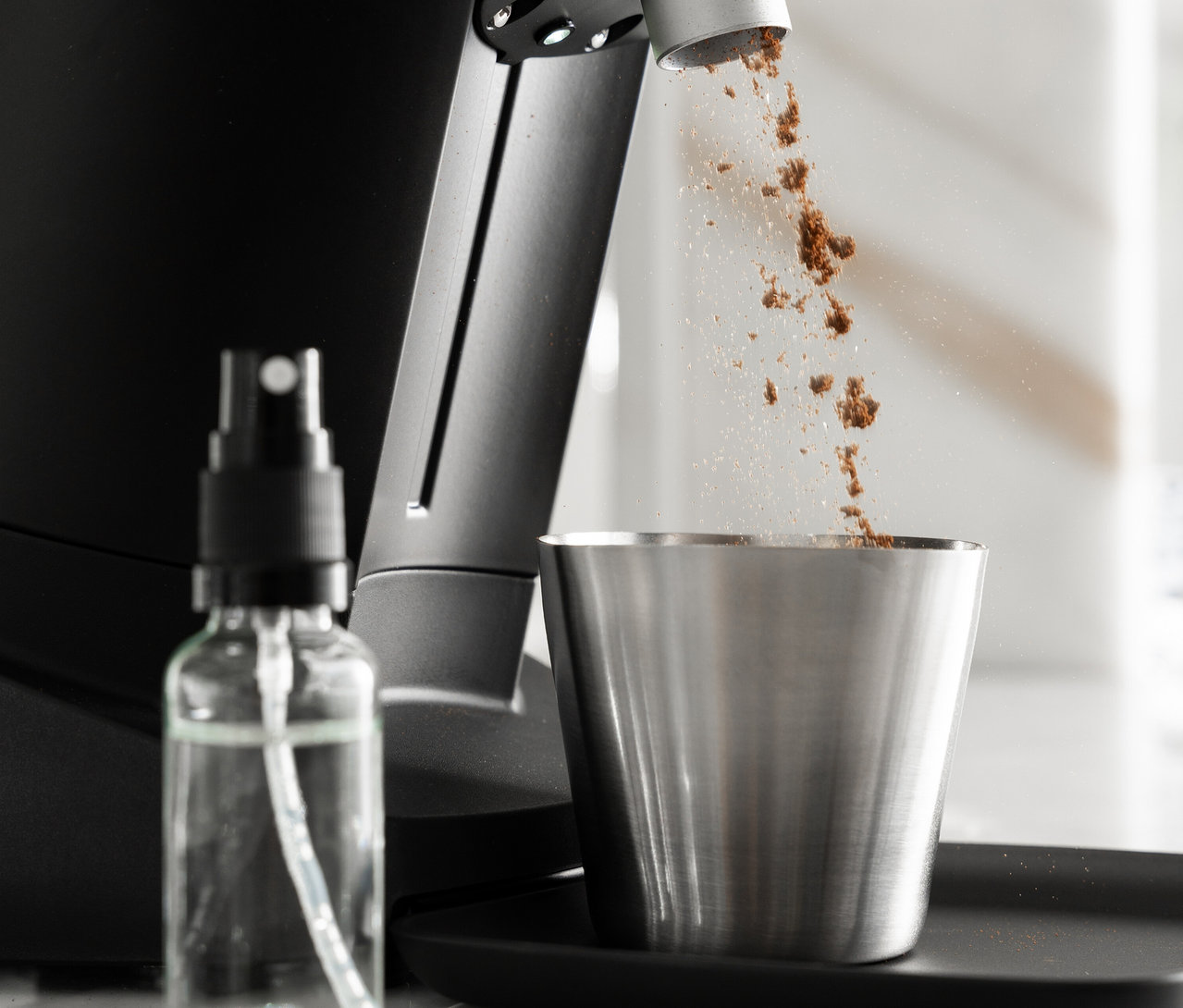 Kaffeepulver wird in einen Edelstahlbecher gefüllt, daneben steht eine Sprühflasche.