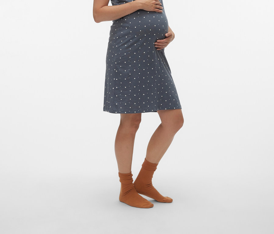 Schwangere Frau trägt ein blaues Umstandskleid mit weißen Punkten und braune Socken.