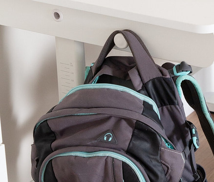 Grauer Rucksack hängt am weißen, höhenverstellbaren Roba Kinderschreibtisch Basic mit Schublade.
