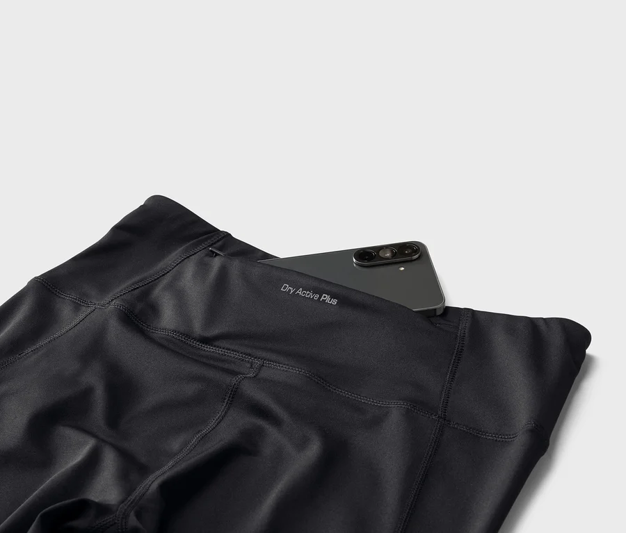Schwarze Leggings mit dem Schriftzug "Dry Active Plus" und einem Smartphone in der Gesäßtasche.