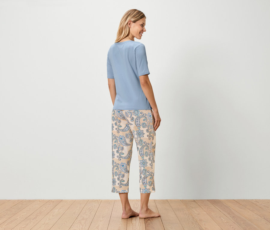 Frau steht mit dem Rücken zur Kamera und trägt ein blaues T-Shirt und eine beige Hose mit blauem Paisleymuster.