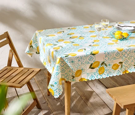 Esstisch mit Zitronenmuster-Tischdecke, Geschirr und Gläsern, daneben ein Holzstuhl.