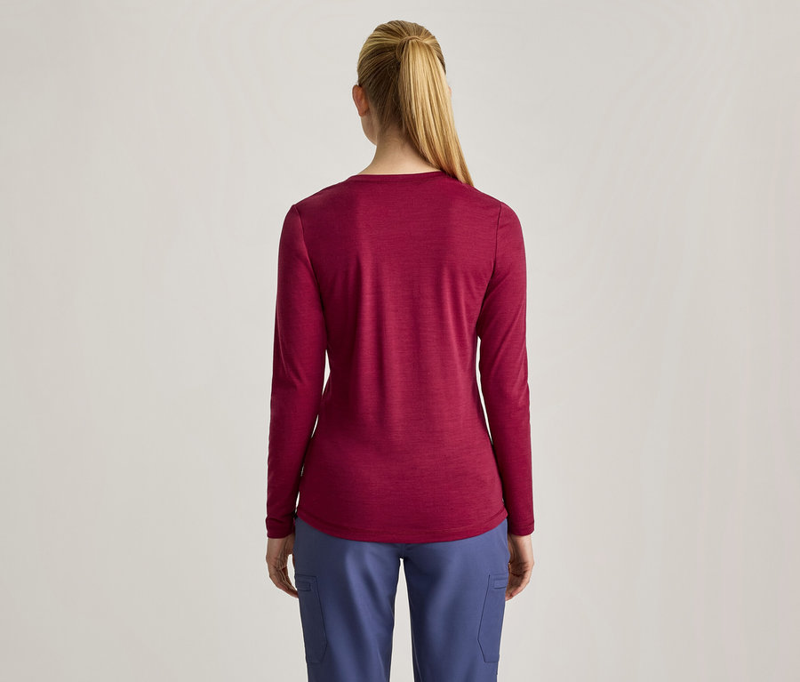 Eine Frau von hinten, die ein langärmeliges, weinrotes Oberteil und blaue Hosen trägt. Ihr blondes Haar ist zu einem Pferdeschwanz gebunden.
