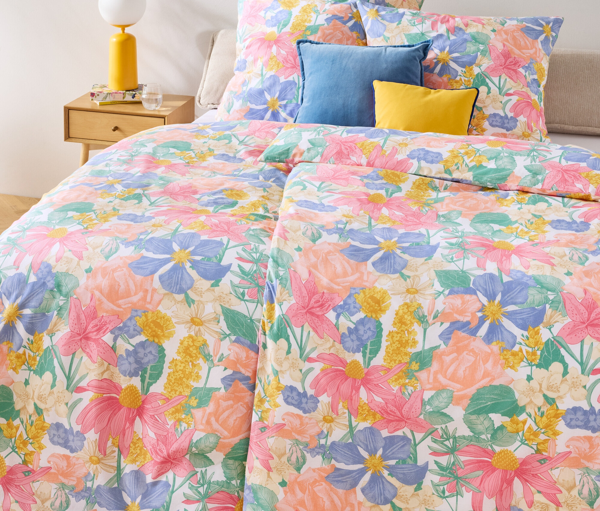 Blumenmuster-Renforcé-Bettwäsche, Doppel-, Normal- und Übergröße auf einem Bett mit blauen und gelben Kissen.
