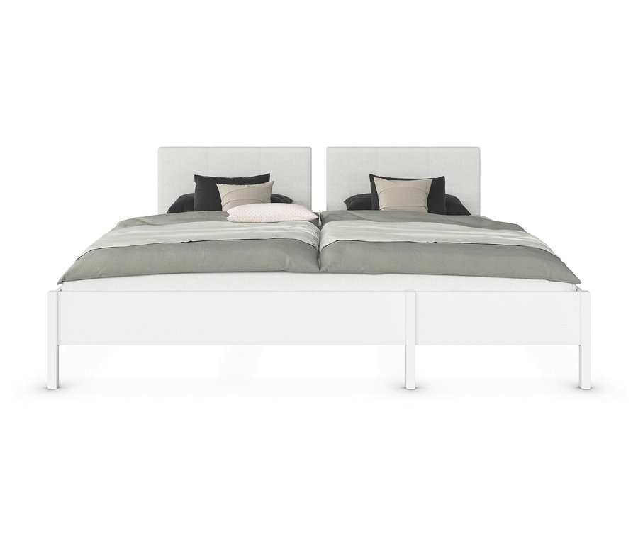 Zwei weiße Betten stehen nebeneinander, jeweils mit einem grauen Bezug, einem schwarzen Kissen und einem gemusterten Kissen.