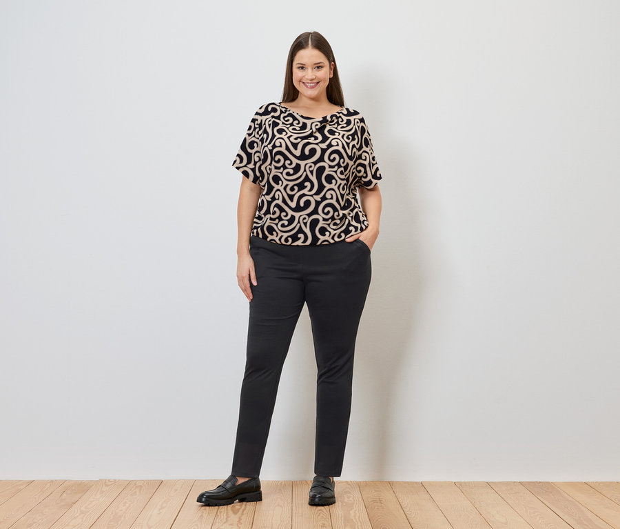 Frau in gemustertem Oberteil und Joggpants mit einer Hand in der Hosentasche.