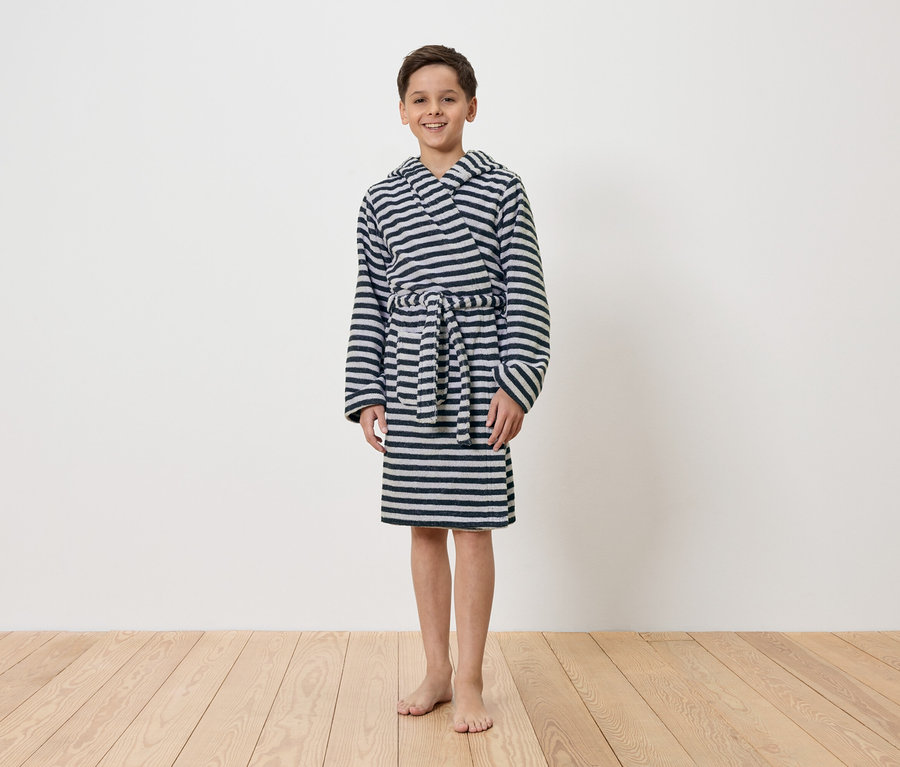 Ein Junge steht barfuß vor einer weißen Wand und trägt einen gestreiften Bademantel mit Kapuze.