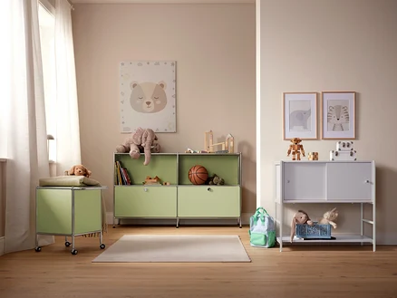 Ein Kinderzimmer mit hellgrünen und weißen Aufbewahrungsschränken, Spielzeug und Bildern an der Wand.